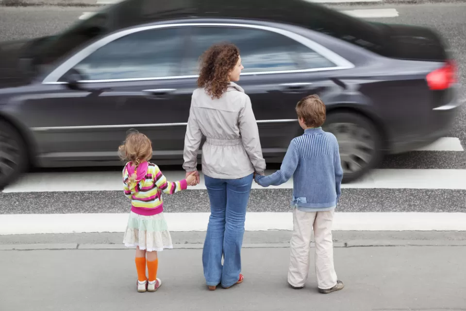 Mother and two young children waiting to cross street at busy crosswalk